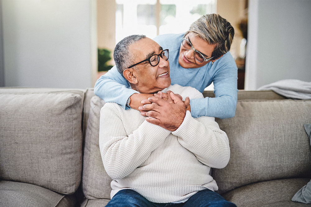 A person on a sofa being embraced by a loved one from behind